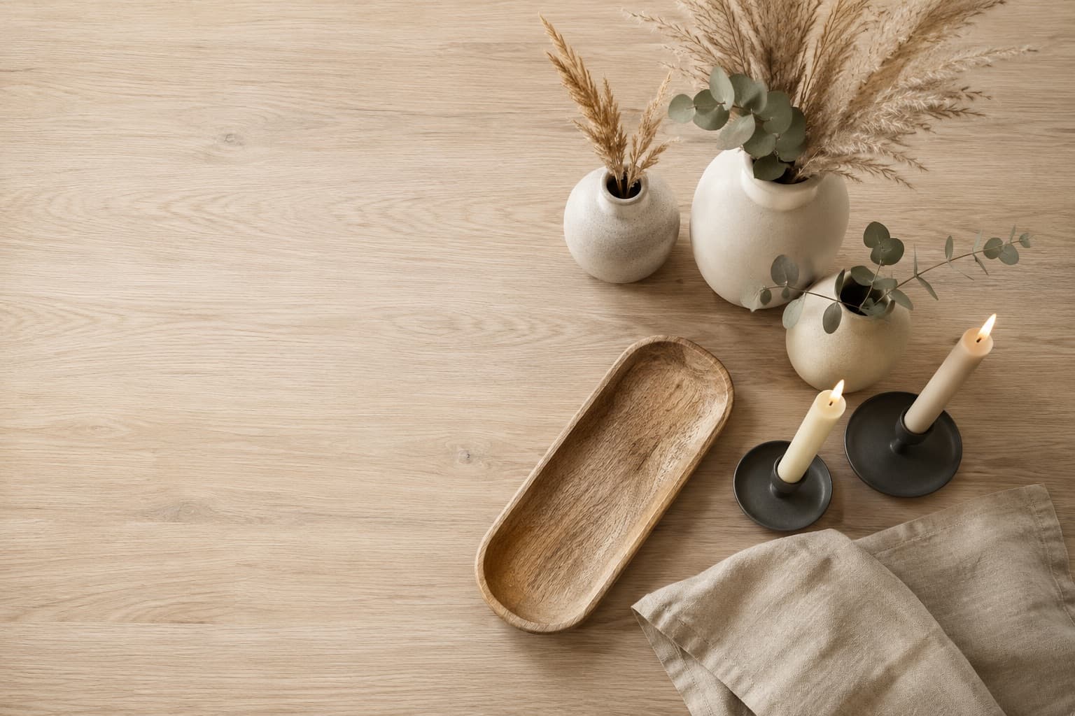 An overhead arrangement of Saini Living decor — ceramic vases, botanical stems, candles and a wooden tray on a pale oak table